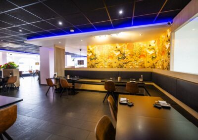 Interieur van Yumi Sushi & Grill in Brunssum met moderne inrichting, sfeervolle verlichting, leren stoelen en een kleurrijke Aziatische muurschildering op de achterwand.