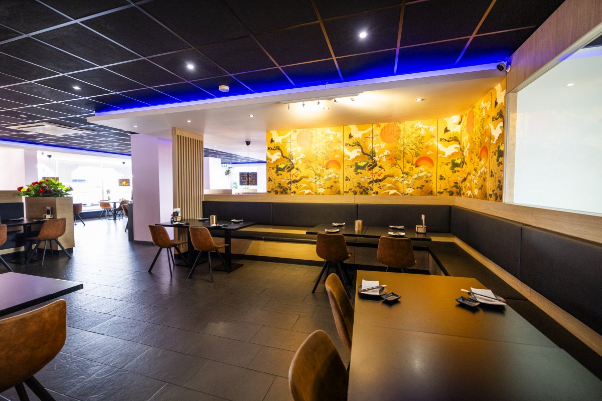 Interieur Interieur van Yumi Sushi & Grill in Brunssum met moderne inrichting, sfeervolle verlichting, leren stoelen en een kleurrijke Aziatische muurschildering op de achterwand.