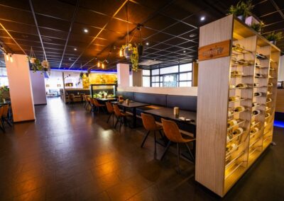 Interieur van Yumi Sushi & Grill met een moderne en warme uitstraling. Het restaurant beschikt over houten tafels, bruine leren stoelen en sfeervolle verlichting. Opvallende elementen is het wijnrek en het aquarium. Hangende planten zorgen voor een stijlvolle en ontspannen ambiance.