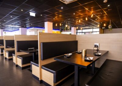Het interieur van Yumi Sushi & Grill straalt een eigentijdse en warme sfeer uit. De comfortabele booth-zitplaatsen met houten panelen en zwarte kussens bieden extra comfort en privacy